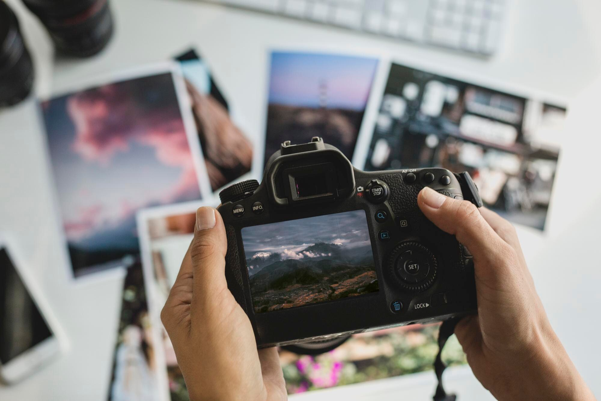 hands-holding-camera-with-photographs-table-photographer-working-his-office